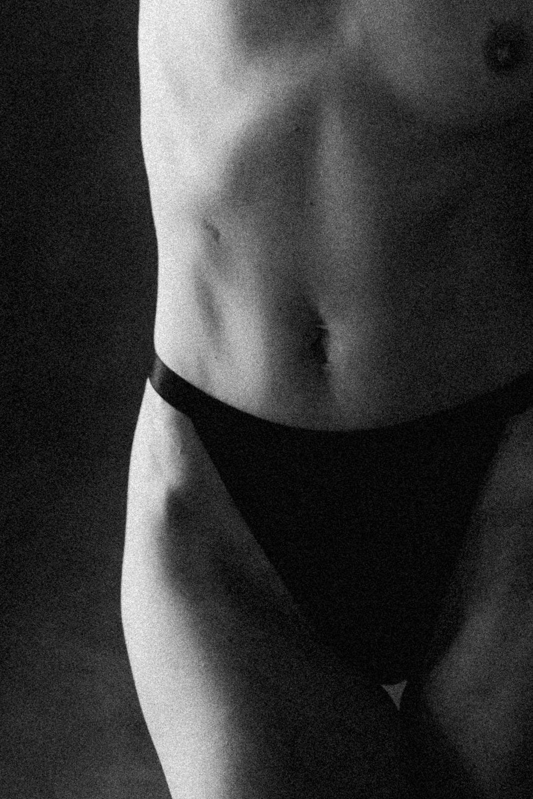 Black and white close-up of a toned torso in black bikini bottoms against a dark background.