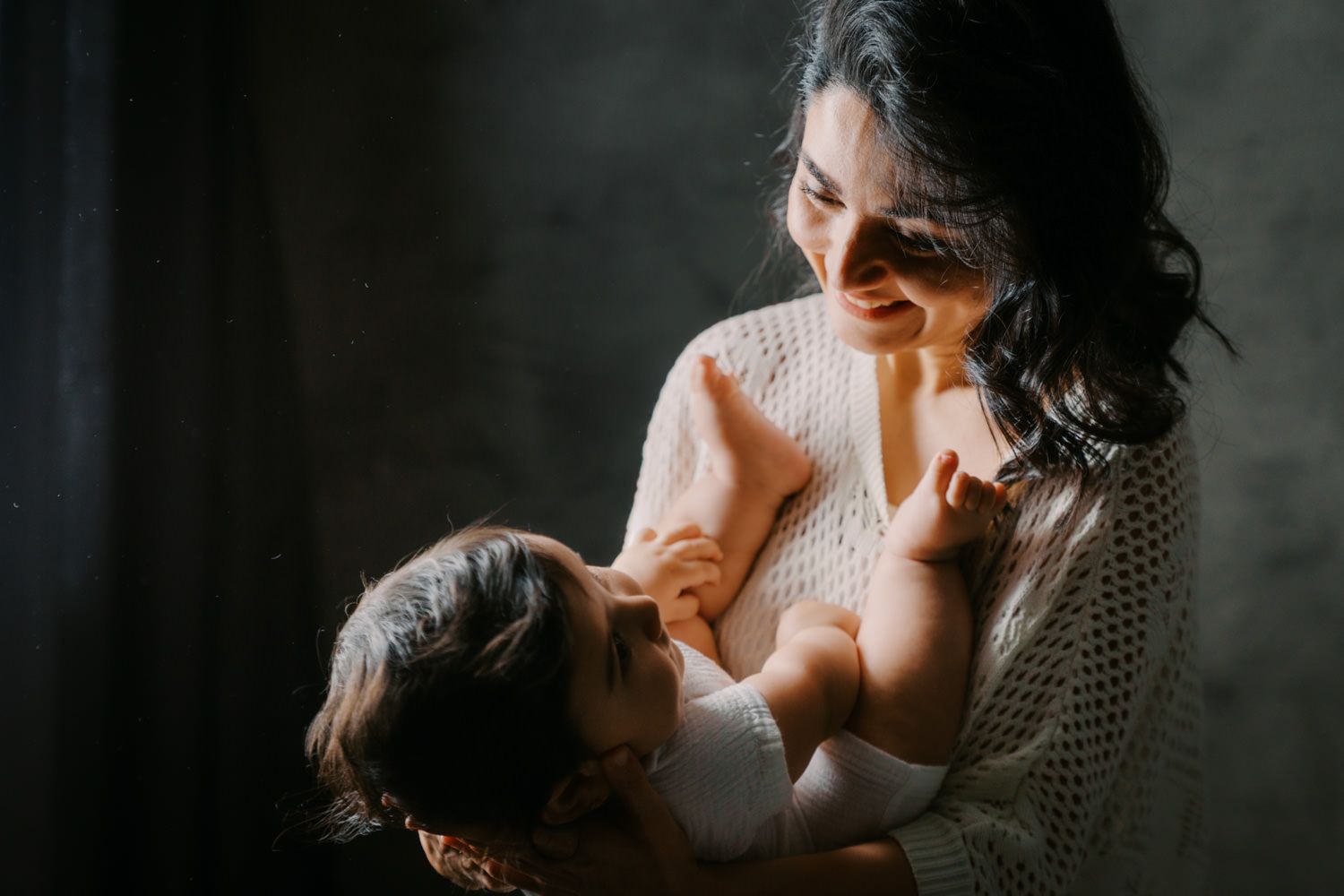 A mother tenderly holds and breastfeeds her newborn baby in soft, natural light.