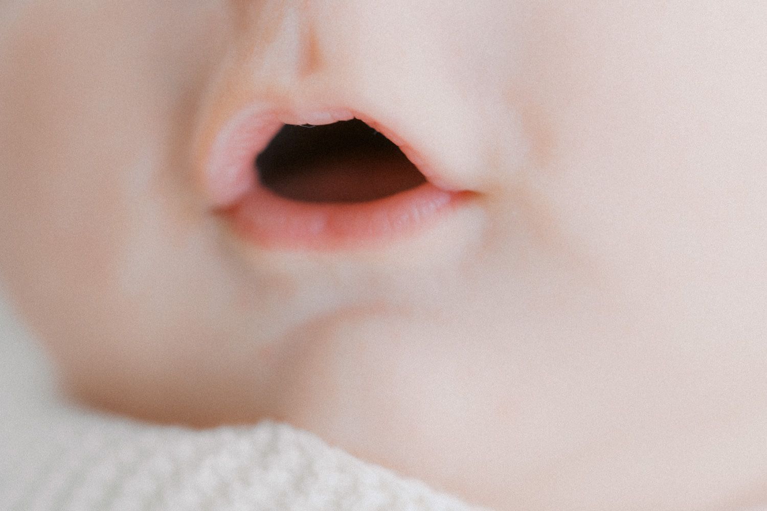 Close-up of a sleeping baby's nose and slightly open lips on a soft white blanket.