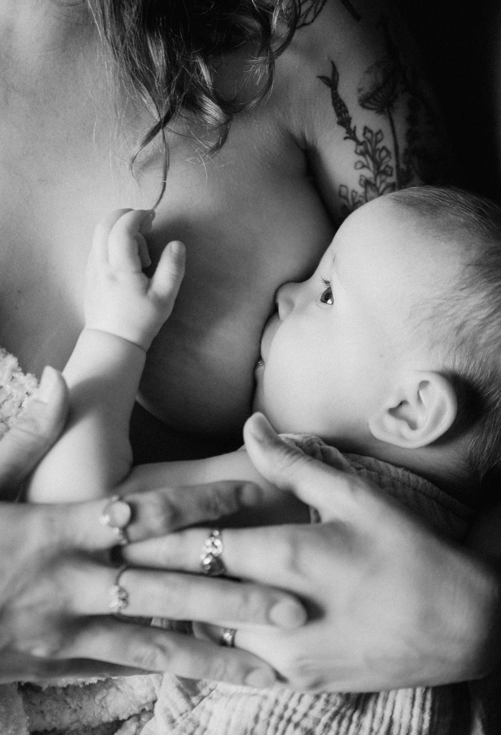 Black and white photo of a mother with tattoos breastfeeding her newborn baby, cradled gently in her hands.