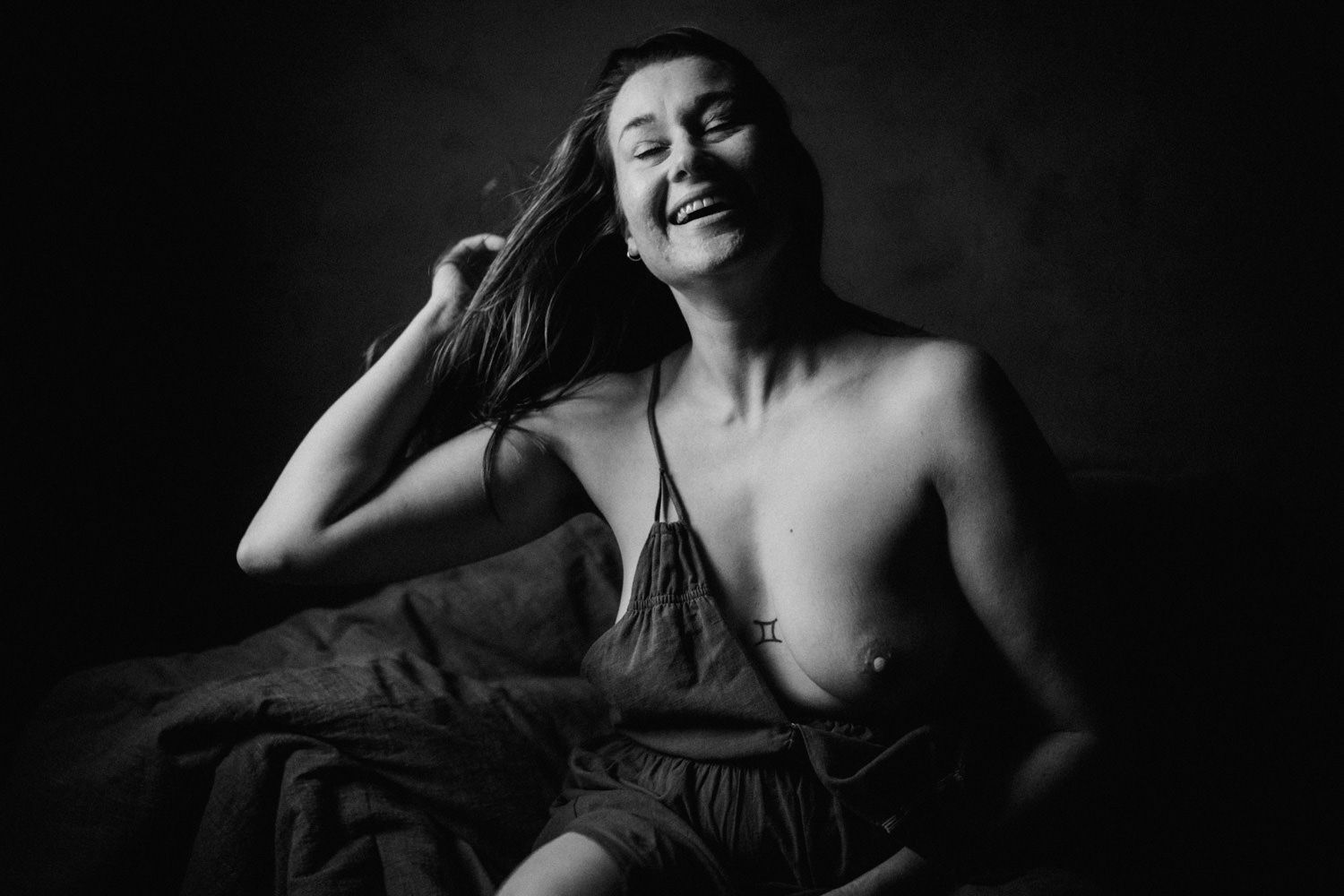 Black and white portrait of a laughing woman with flowing hair, sitting relaxed in a candid artistic photo.