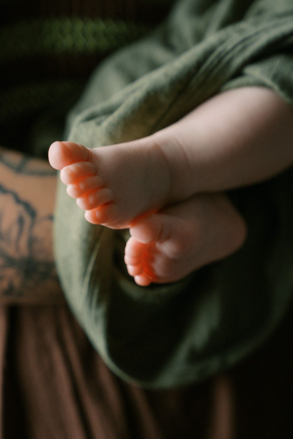 Close-up of tiny newborn baby feet resting on a green fabric blanket.