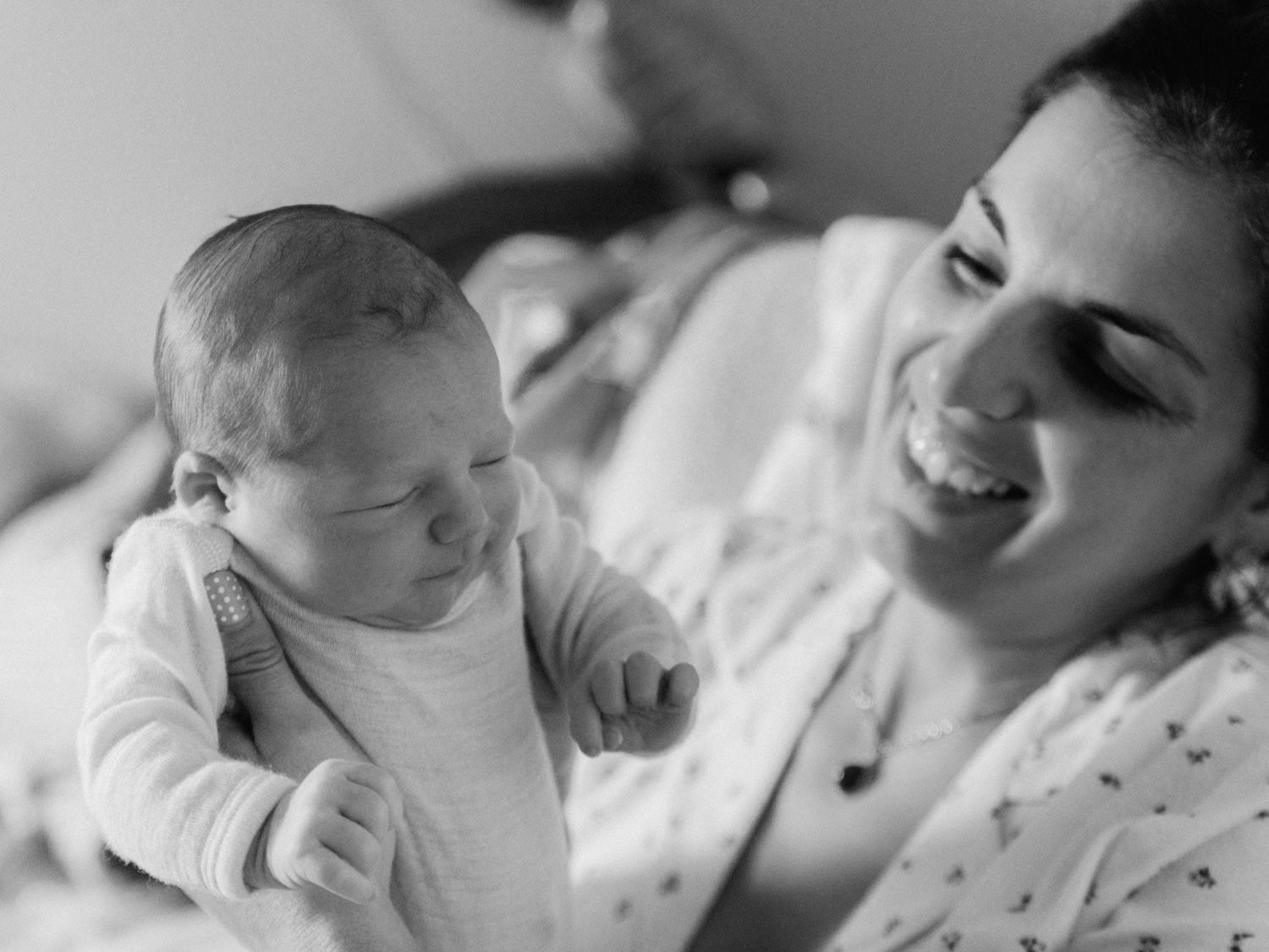 Black and white photo of a smiling mother holding her newborn baby in a hospital room after birth.