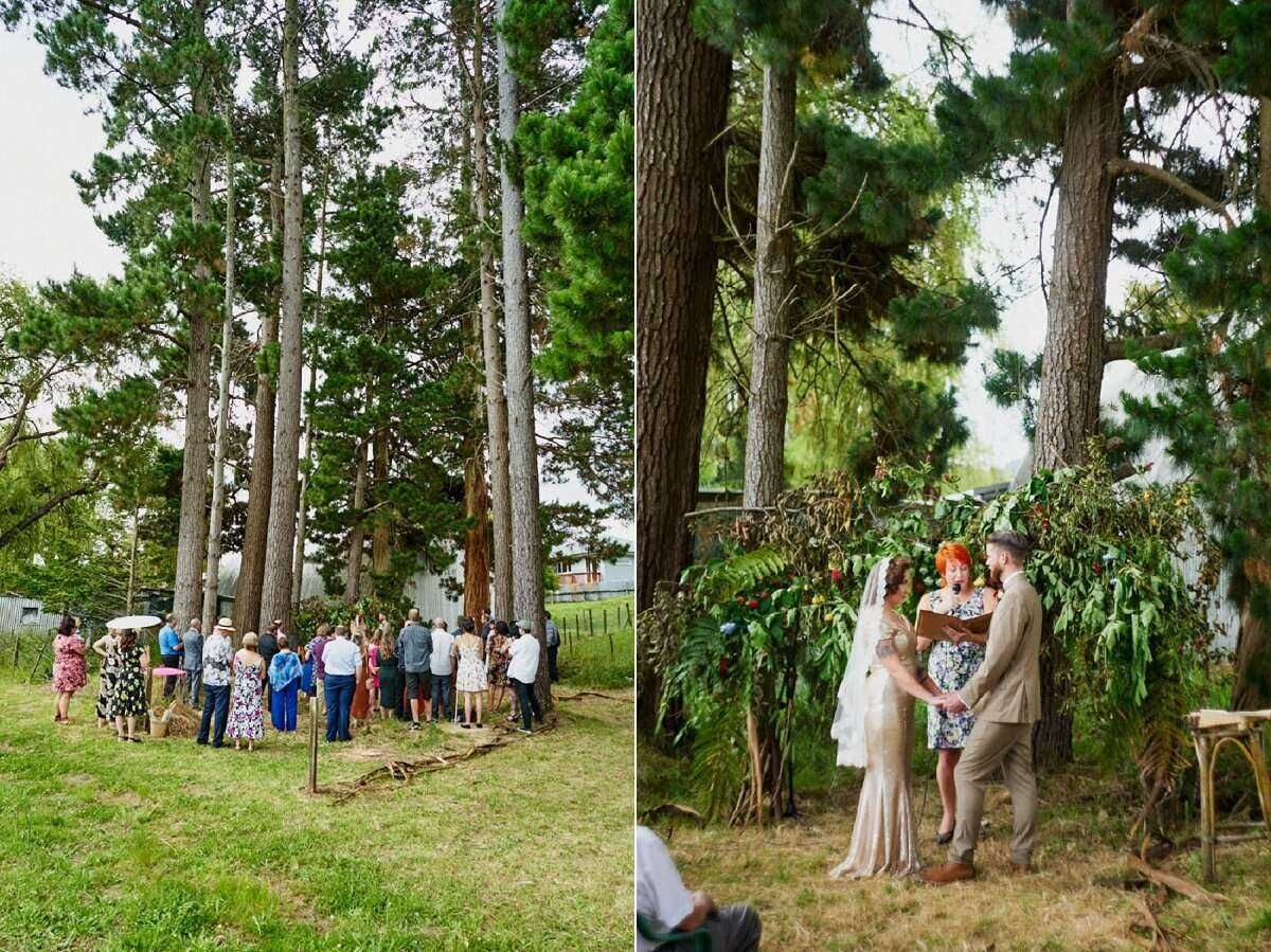 Outdoor wedding ceremony under tall pine trees with guests gathered on grass and couple exchanging vows beneath floral arch.