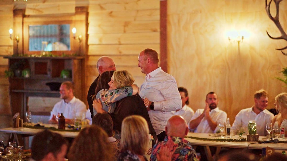 Guests applaud as a couple shares a warm embrace during a rustic wedding reception dinner in a cozy log cabin venue.