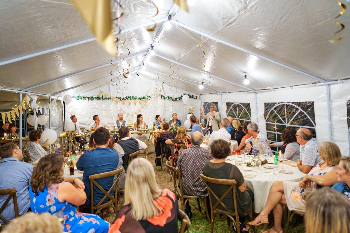 Guests dining under a white tent at an elegant outdoor wedding reception with decorative lighting.