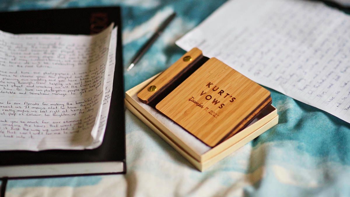 Wooden notepad holder labeled Kurt's Vows sits on a desk beside open journals and handwritten notes.