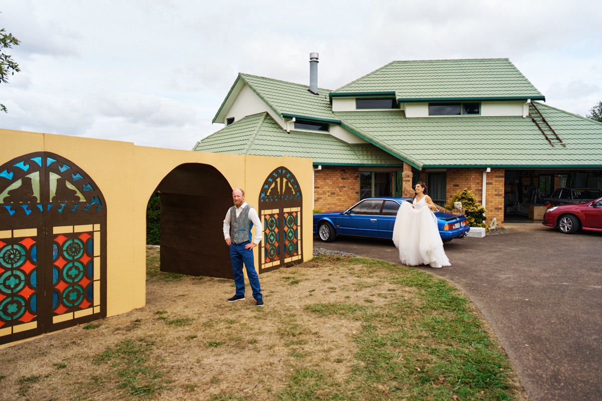 Bride and groom pose outside a brick venue with colorful stained glass gates and green roof on their wedding day.