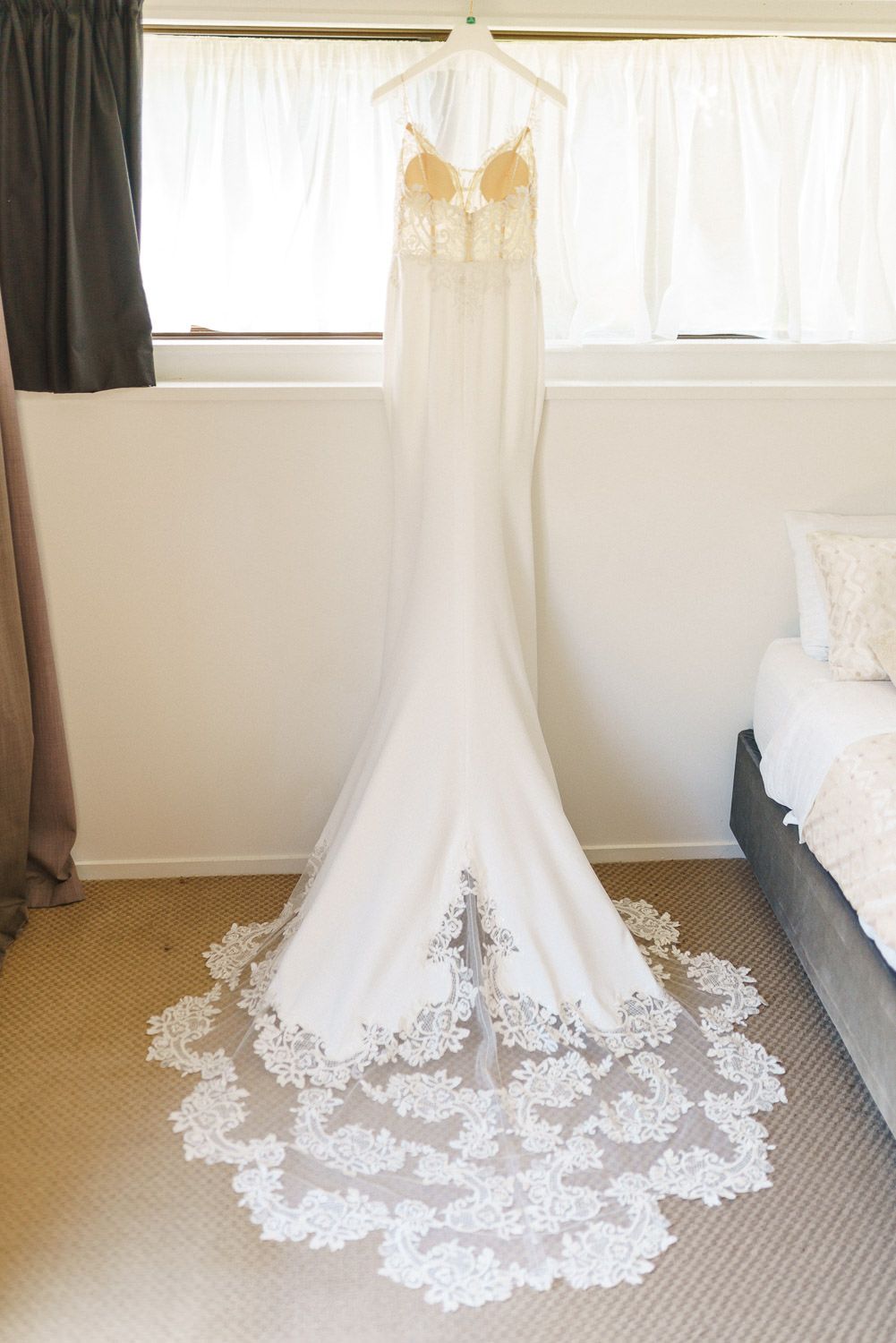 Elegant white wedding dress with gold lace bodice and cathedral train hanging in a bright bedroom.