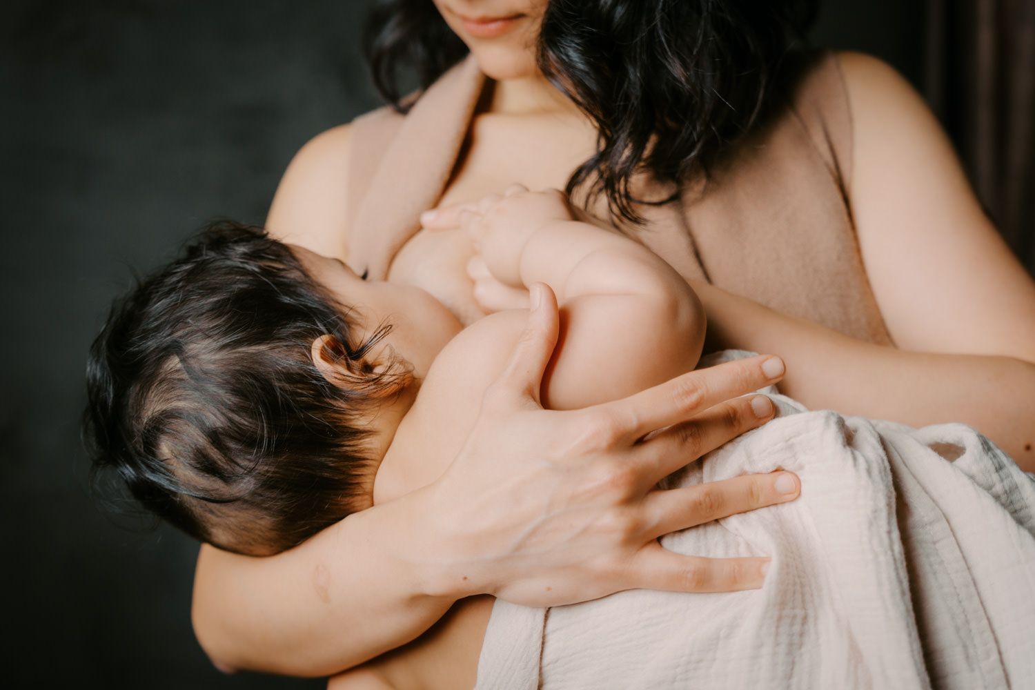 A mother tenderly breastfeeds her newborn baby, wrapped in a soft blanket, in a warm and intimate setting.