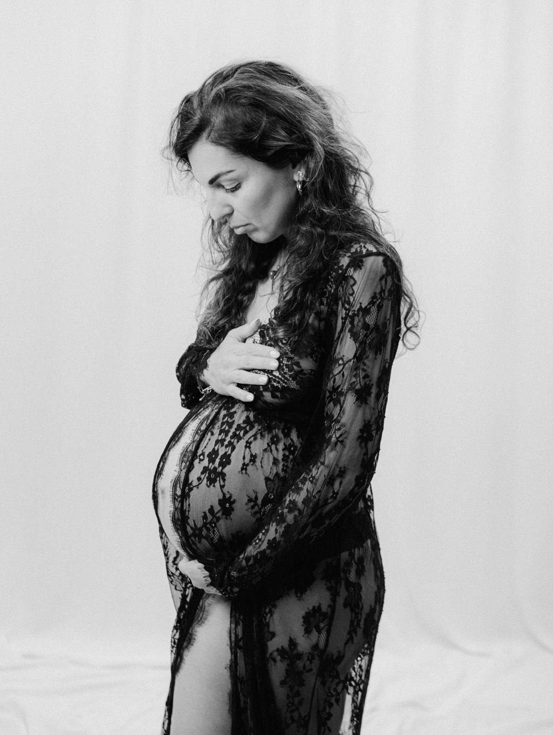 Black and white maternity photo of pregnant woman in black lace gown.
