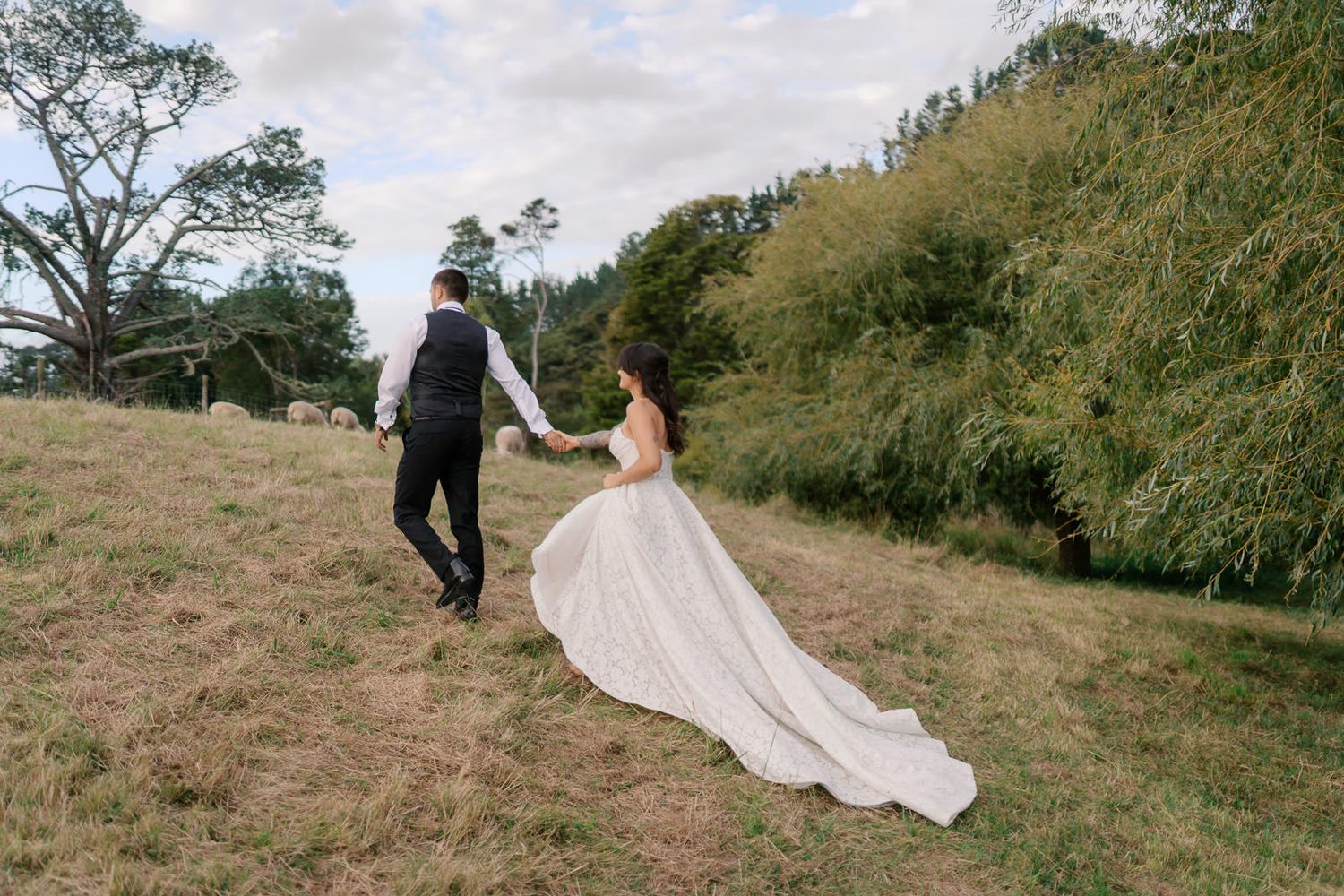 Bride and groom walking hand in hand through a lush green hillside on their wedding day.