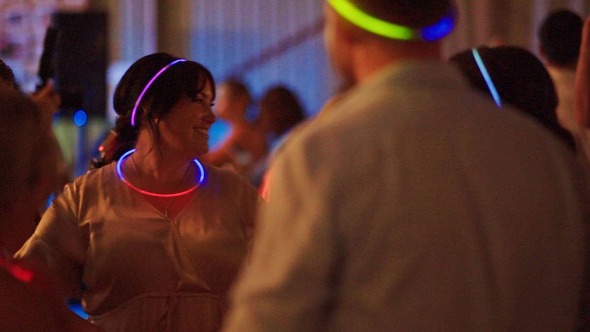 People dancing at a party wearing colorful glowing neon headbands and necklaces in a festive venue.