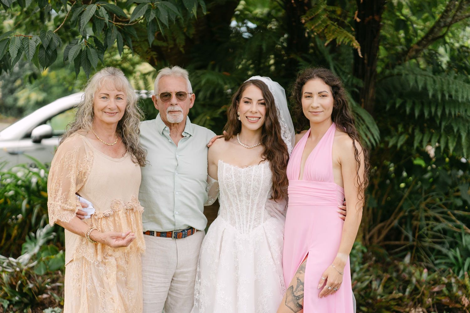 A bride poses with three family members outdoors at a wedding celebration.