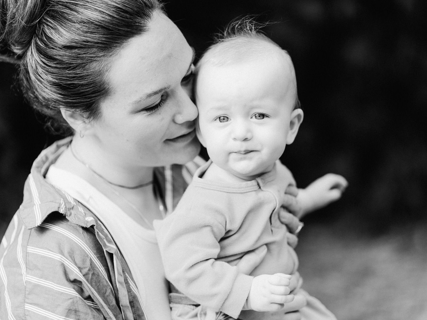 Black and white photo of a young mother tenderly holding her smiling baby outdoors.