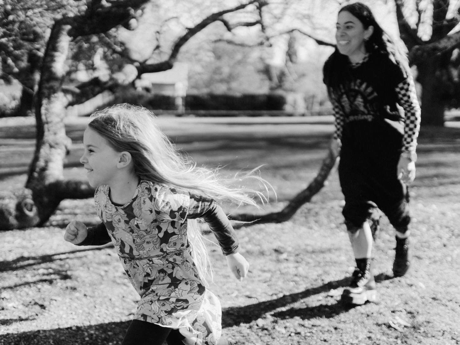 Black and white photo of two girls running and playing together in a sunlit park.