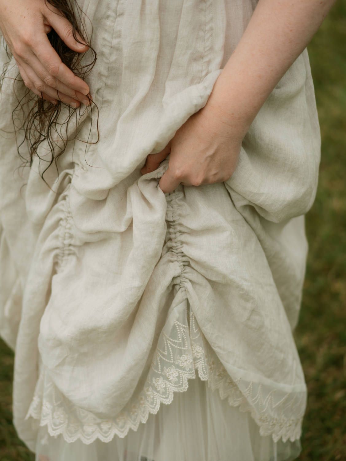Woman in ivory linen dress with lace trim gathering fabric, vintage romantic style bridal fashion.