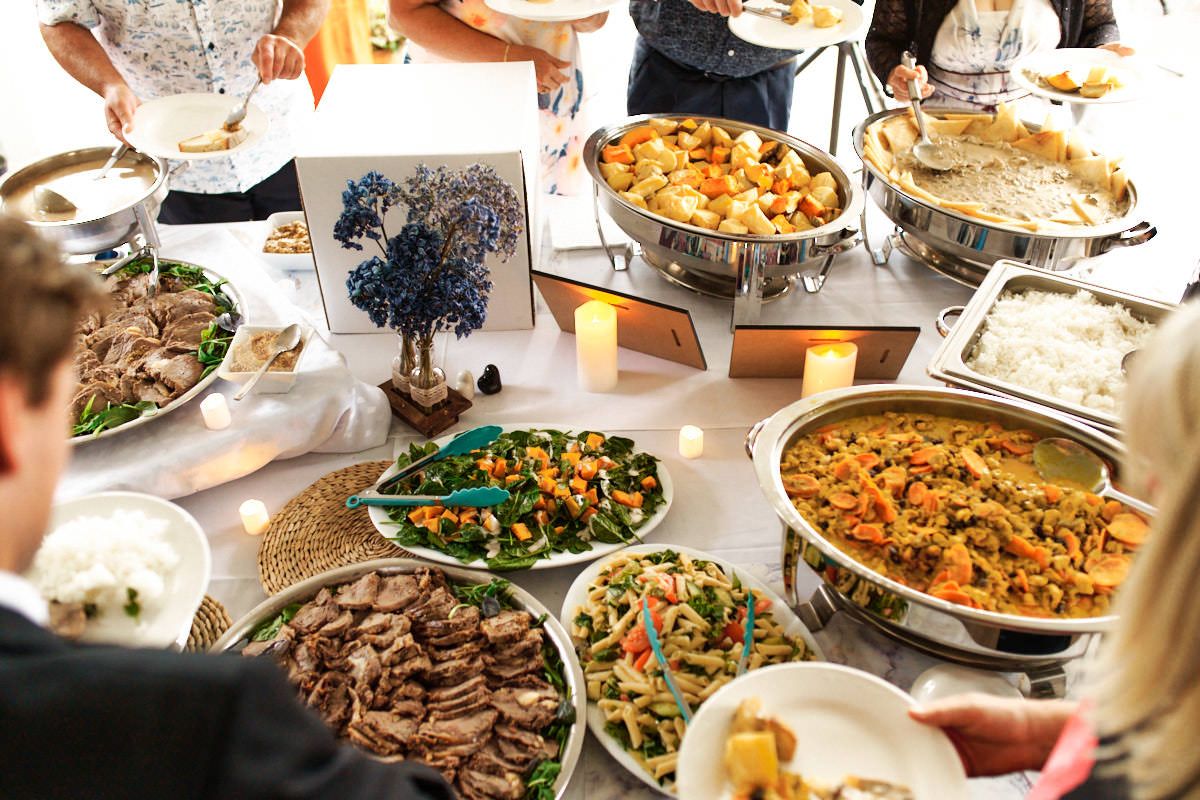 Guests serving themselves at an elegant buffet table filled with colorful dishes and warm chafing dishes at a catered event.