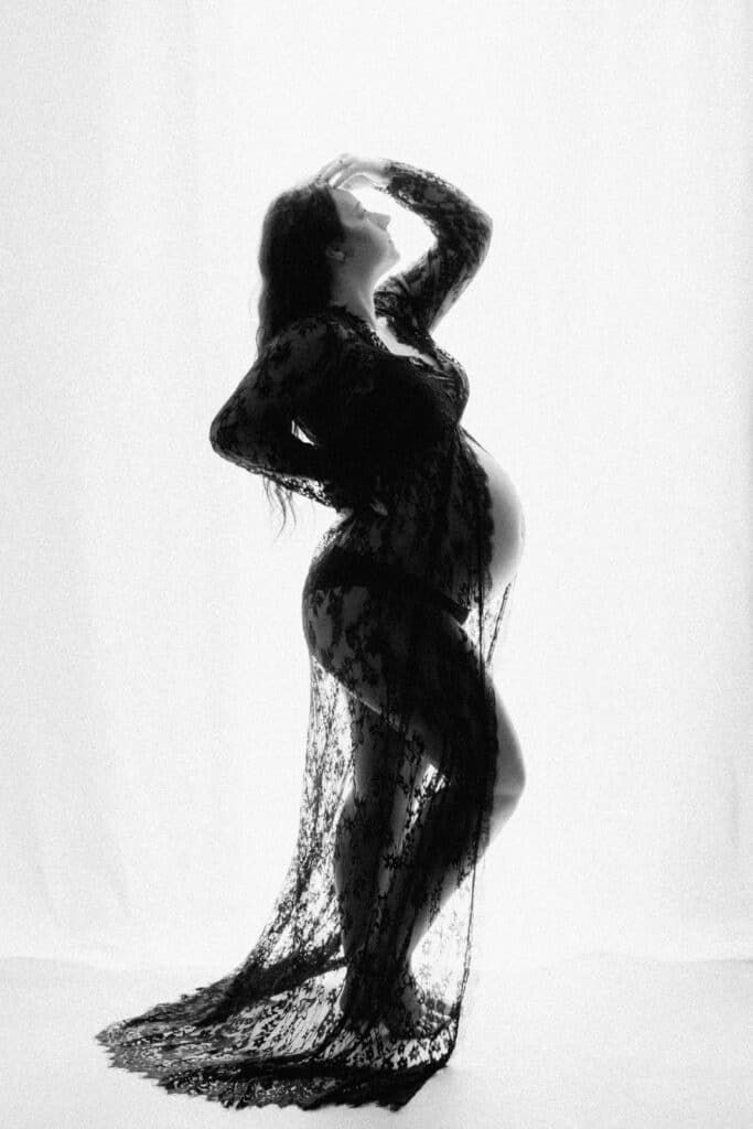 Black and white silhouette of a pregnant woman in lace robe posing gracefully against a white background.