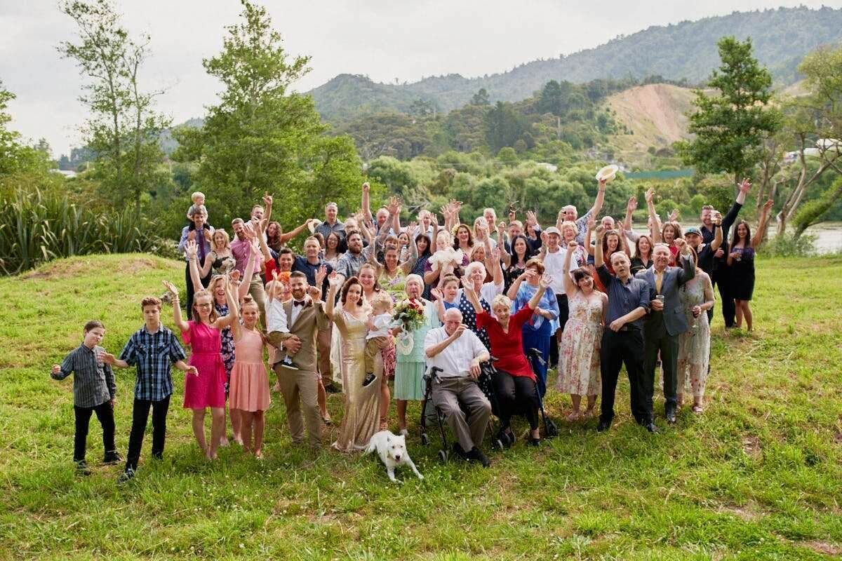 Large family group photo outdoors on green grass with lush hills and a lake in the background.