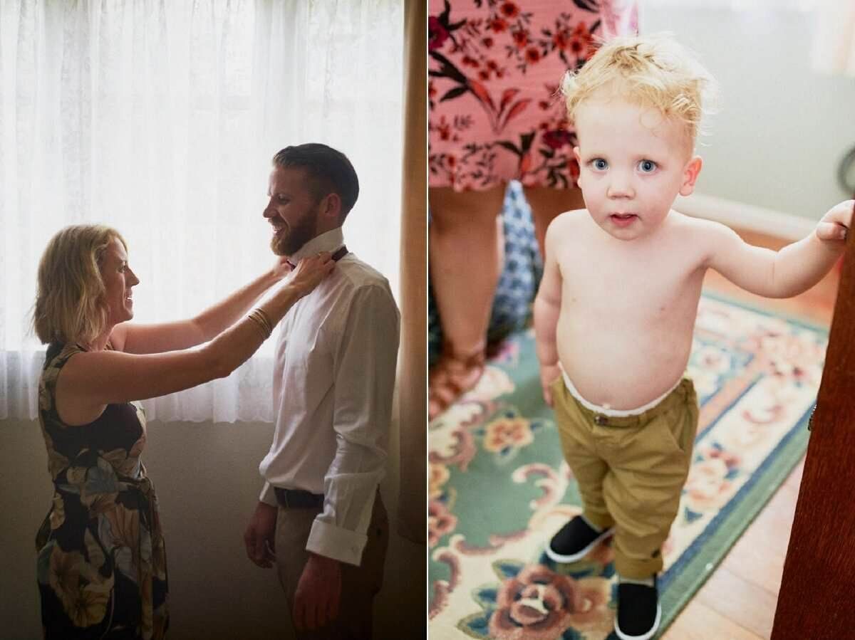 Woman adjusting man's collar indoors; toddler boy in khaki pants standing on a colorful rug.