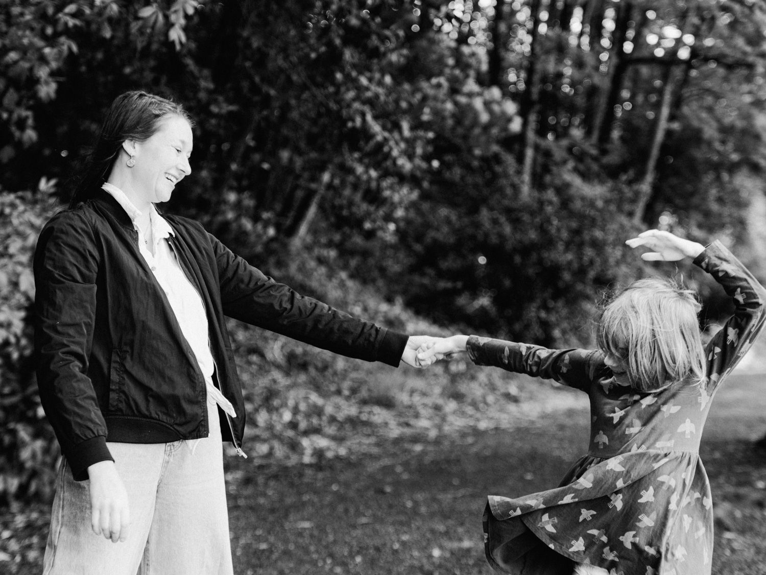 Black and white photo of two women holding hands outdoors, spinning together in a garden setting.