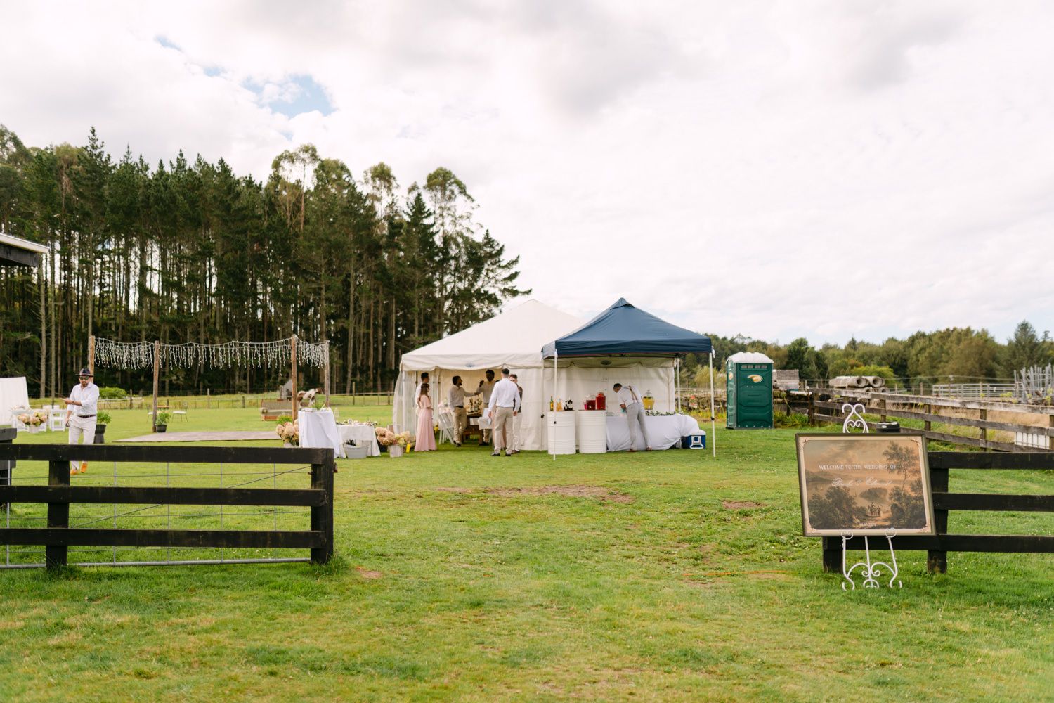 Outdoor farm event setup with white marquee tent, gazebo, and rustic wooden fencing on lush green grass.