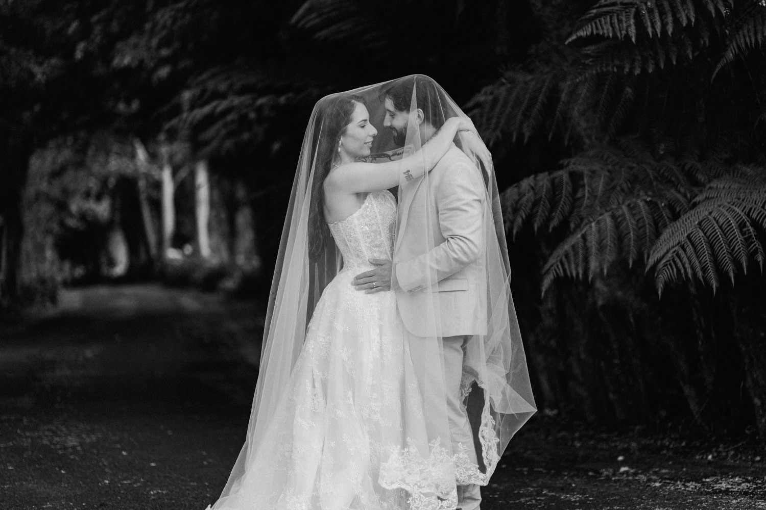 Black and white photo of a bride and groom sharing an intimate moment under her flowing veil outdoors.