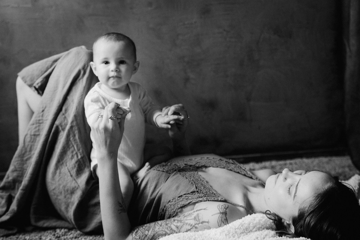 Black and white photo of a mother lying down while lovingly holding her smiling baby up in the air.