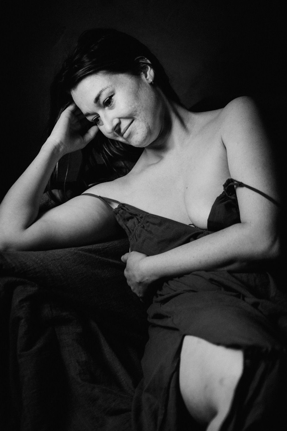 Black and white portrait of a woman in lingerie posed against a dark background.
