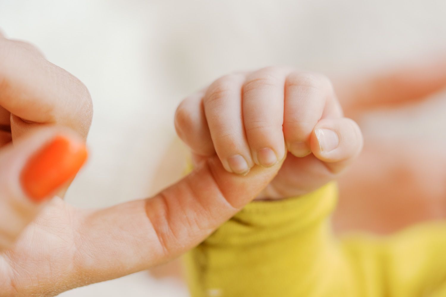 A newborn baby grasping an adult finger, wearing a yellow outfit, with a close-up view of tiny hands.