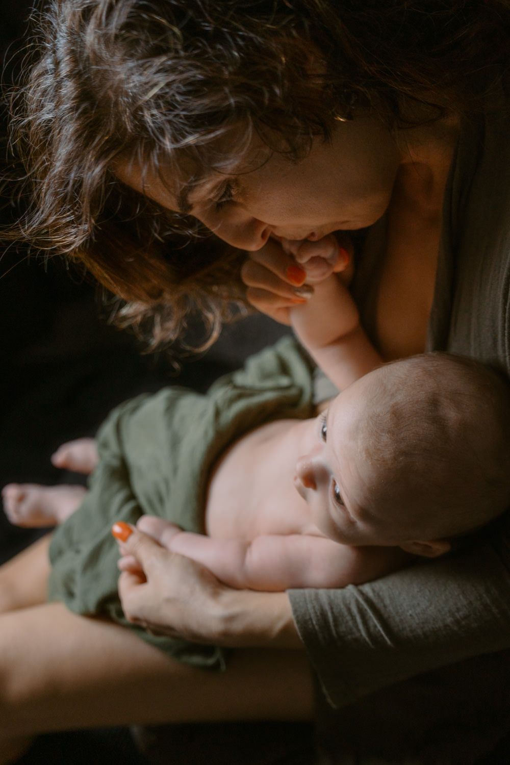 A mother tenderly gazes at her newborn baby wrapped in a green cloth in a warm, intimate moment.