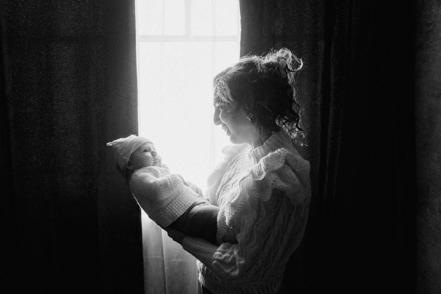 Black and white photo of a mother cradling her newborn baby by a sunlit window.