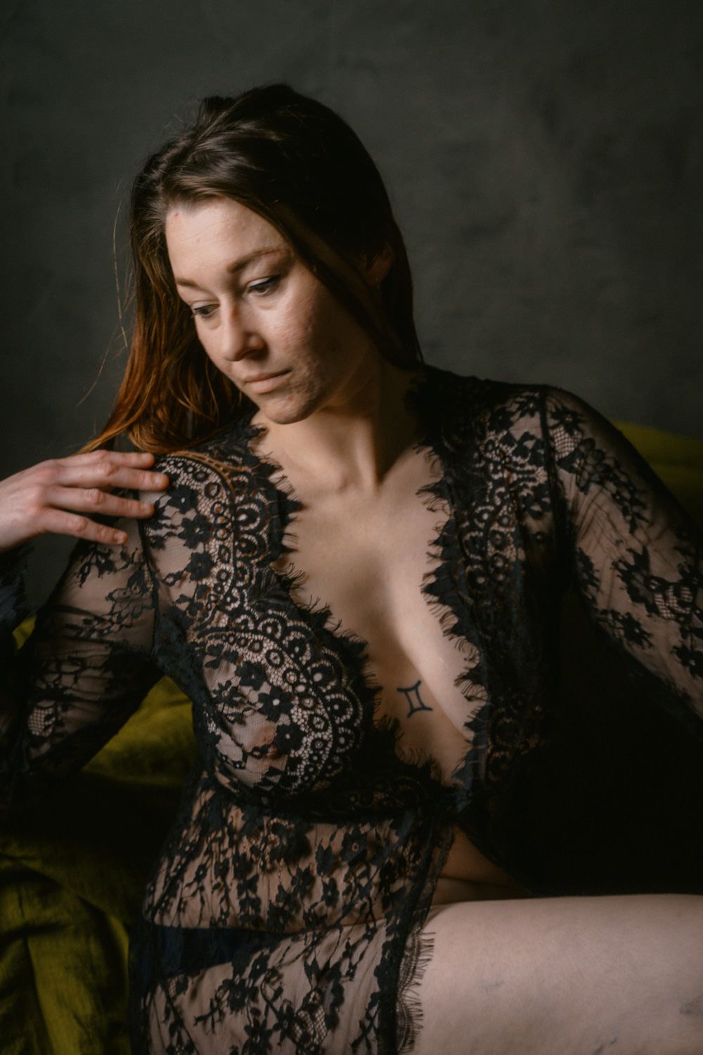 Woman in black lace lingerie dress posing elegantly against a dark moody background in a boudoir setting.
