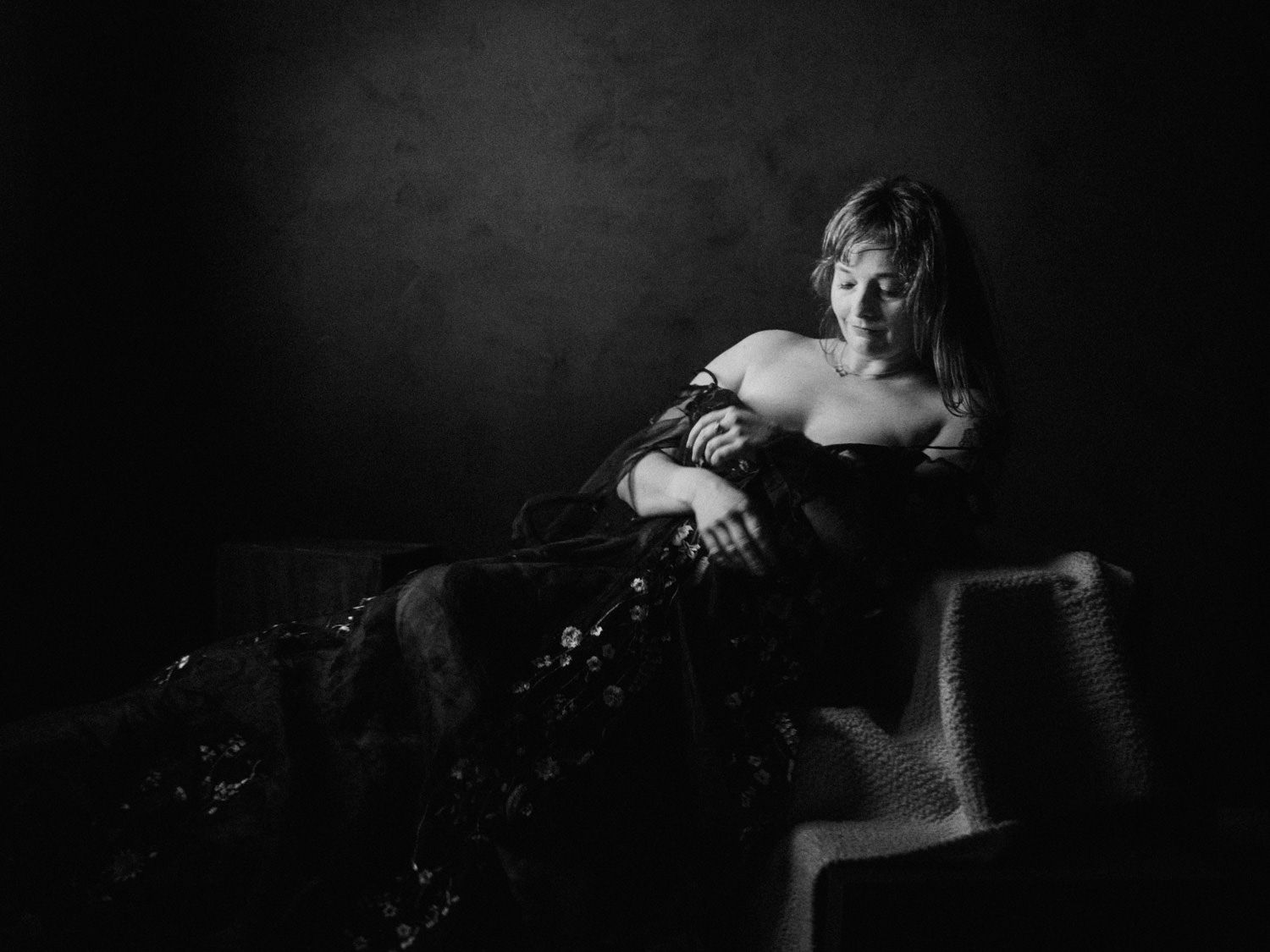 Elegant black and white portrait of a woman in a strapless gown reclining gracefully on a chair.
