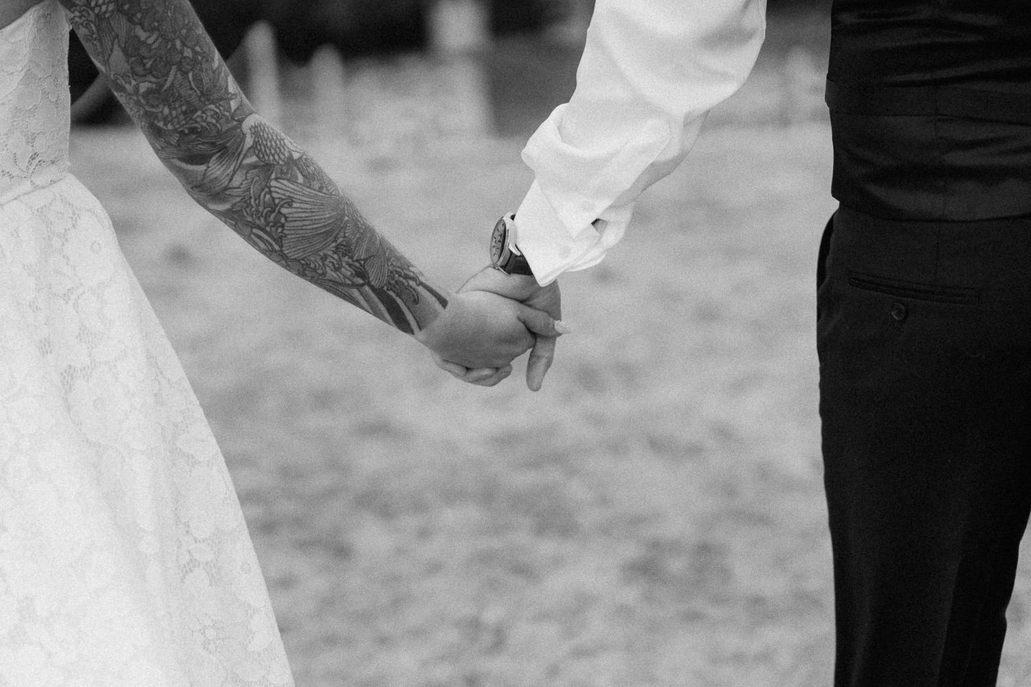 Black and white photo of bride and groom holding hands at wedding ceremony, bride in lace dress.