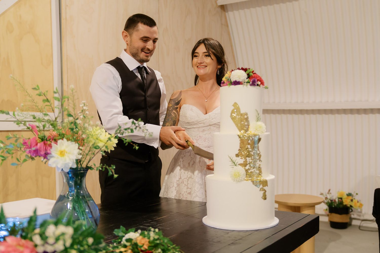 Bride and groom smiling while cutting their elegant white and gold wedding cake at their wedding reception.