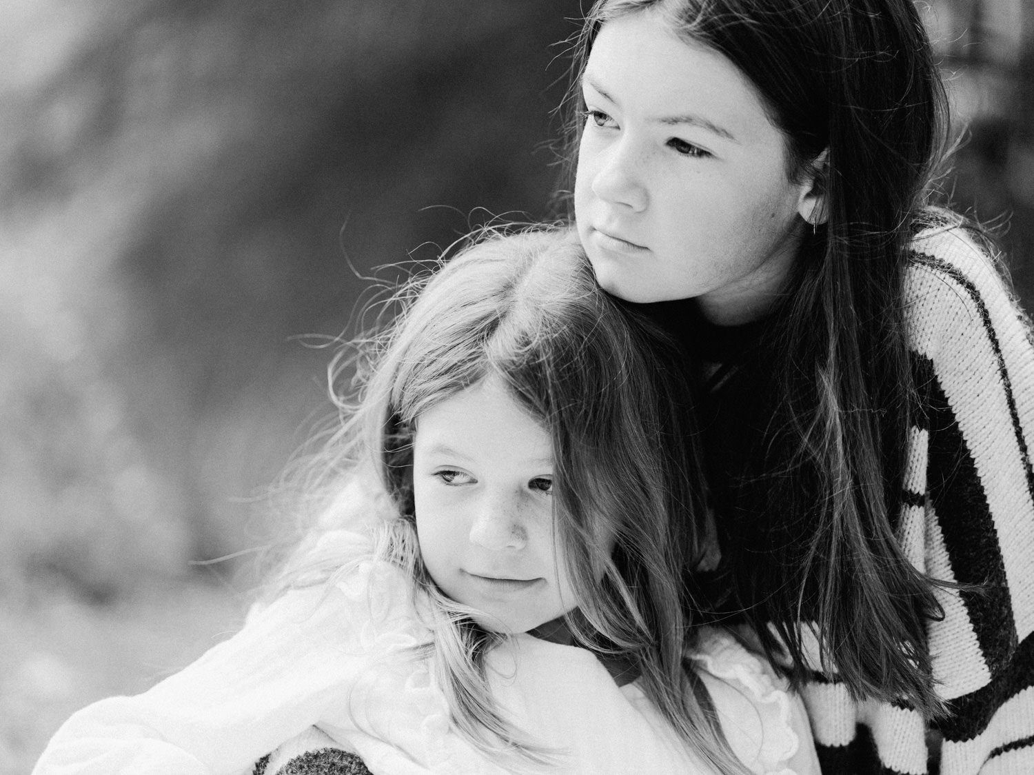 Black and white portrait of two young girls, older sister embracing younger child outdoors.