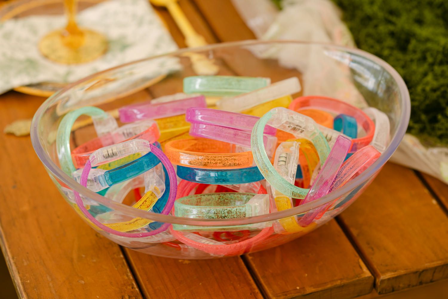 Colorful plastic wristbands and bracelets displayed in a clear bowl at a party or event.