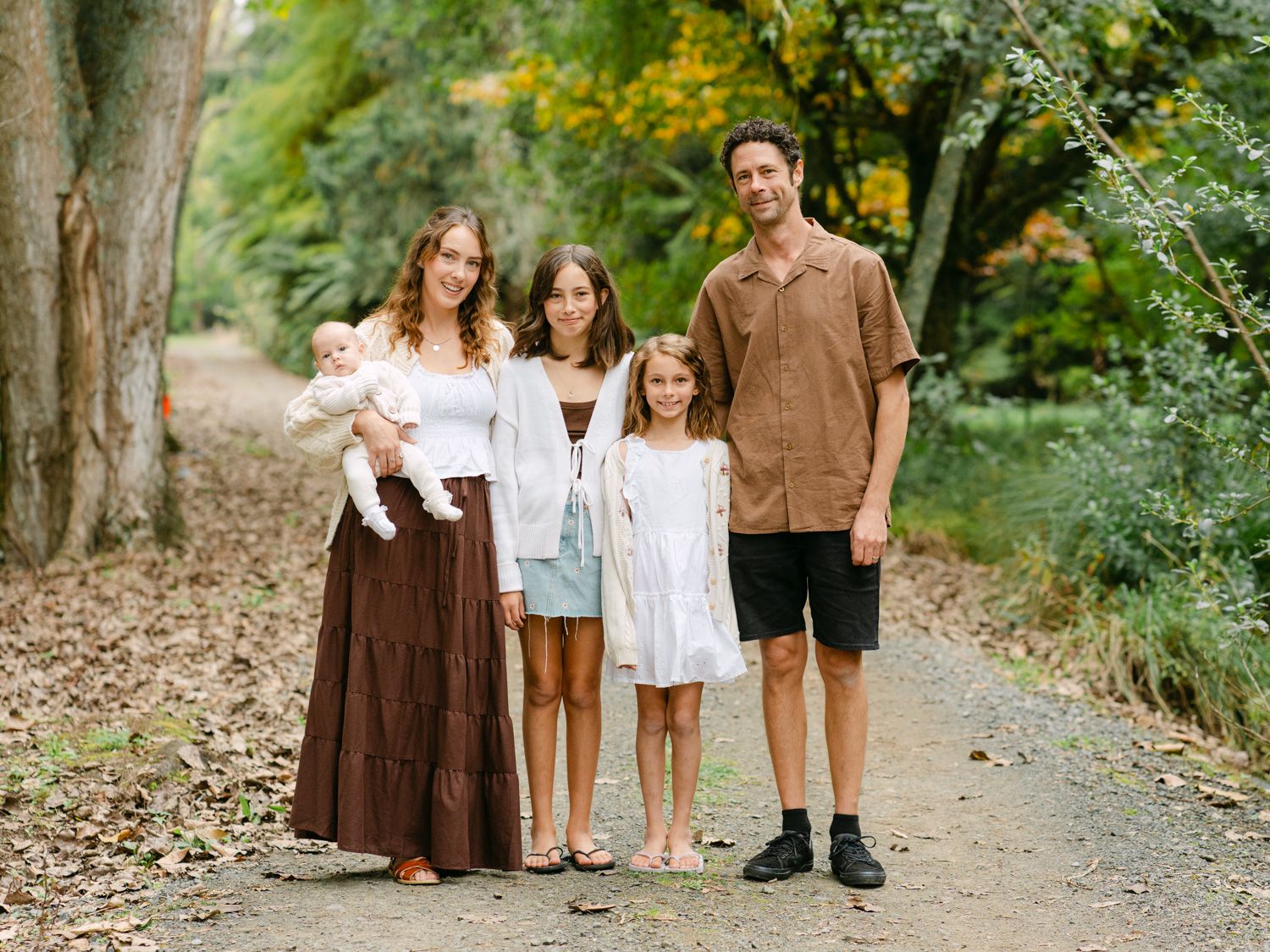 Family of five posing on a scenic forest path surrounded by lush green and yellow foliage.