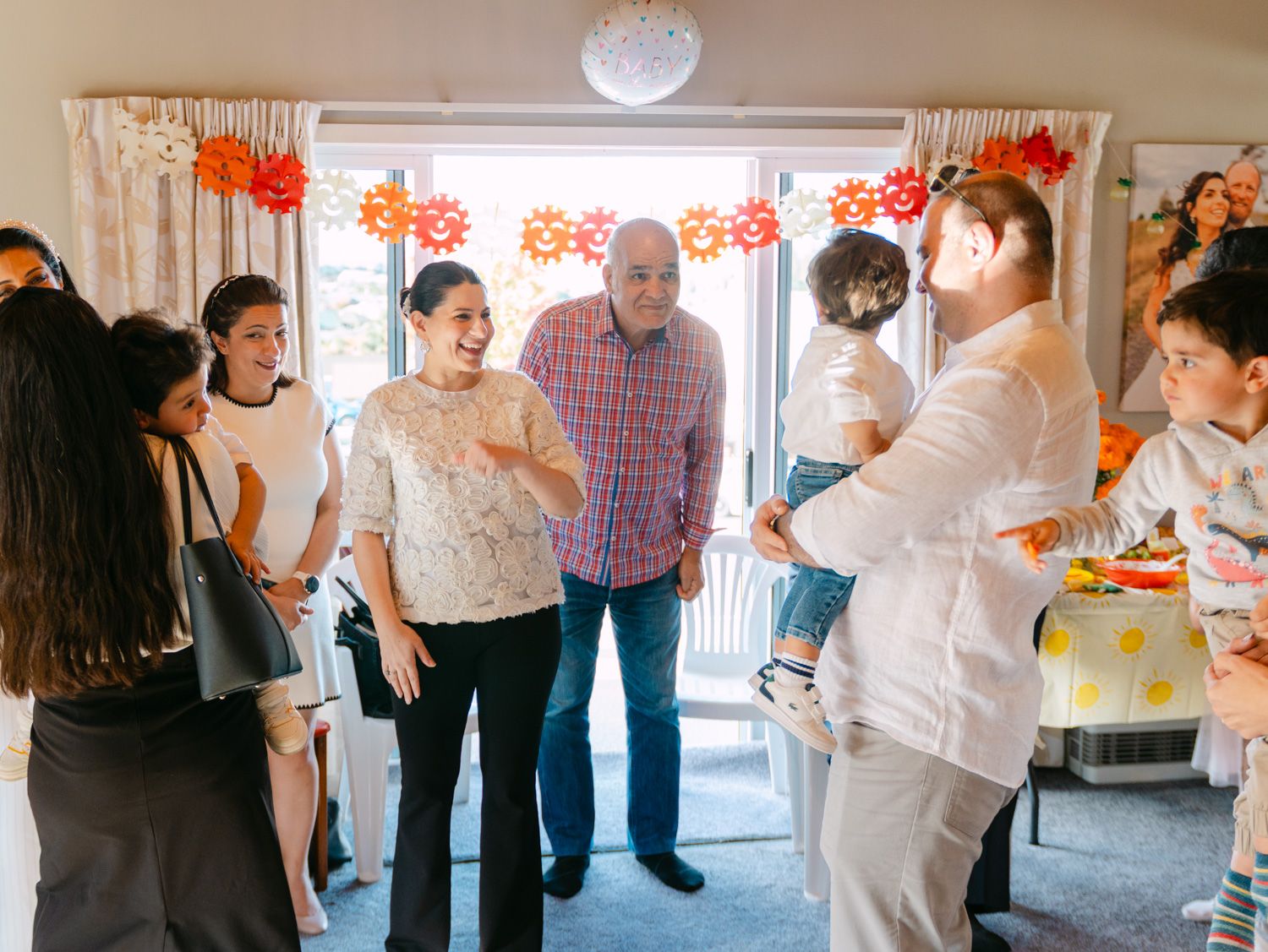 Family gathering indoors with colorful paper flower decorations, guests socializing at a casual celebration party.