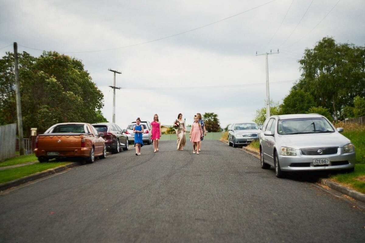 Group of women in colorful dresses walking down a quiet suburban street lined with parked cars.