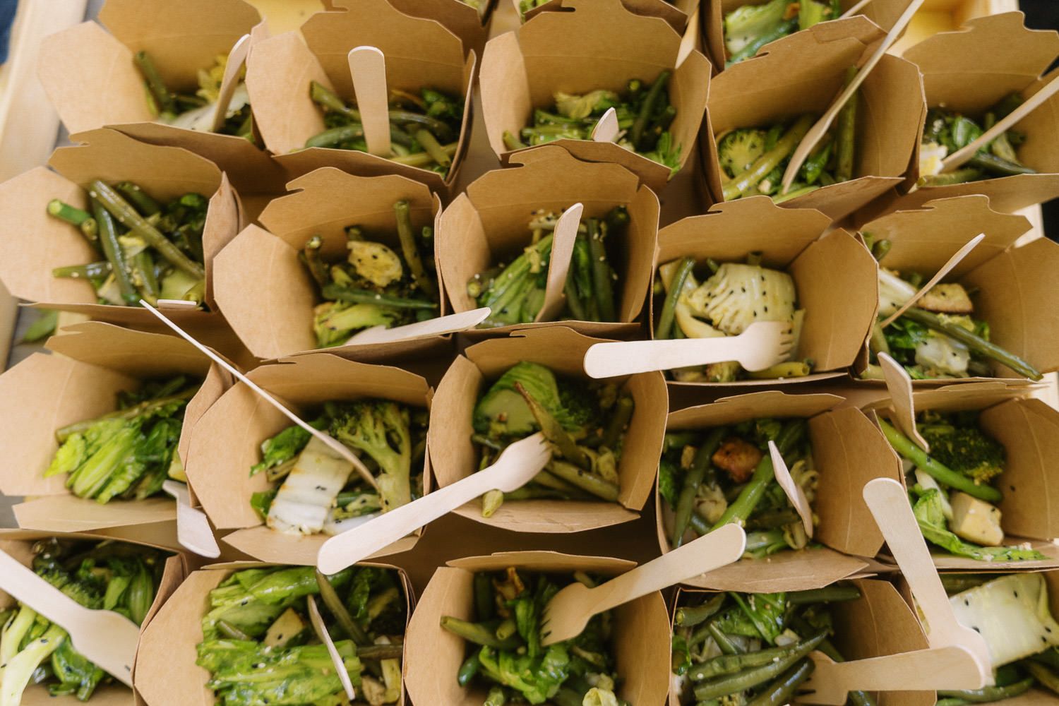 Eco-friendly kraft paper boxes filled with fresh green asparagus and vegetables, served with wooden forks at a catered event.