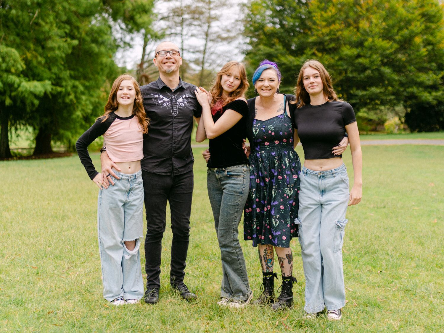 Group of five people smiling outdoors in a green park, posing together on a sunny day.