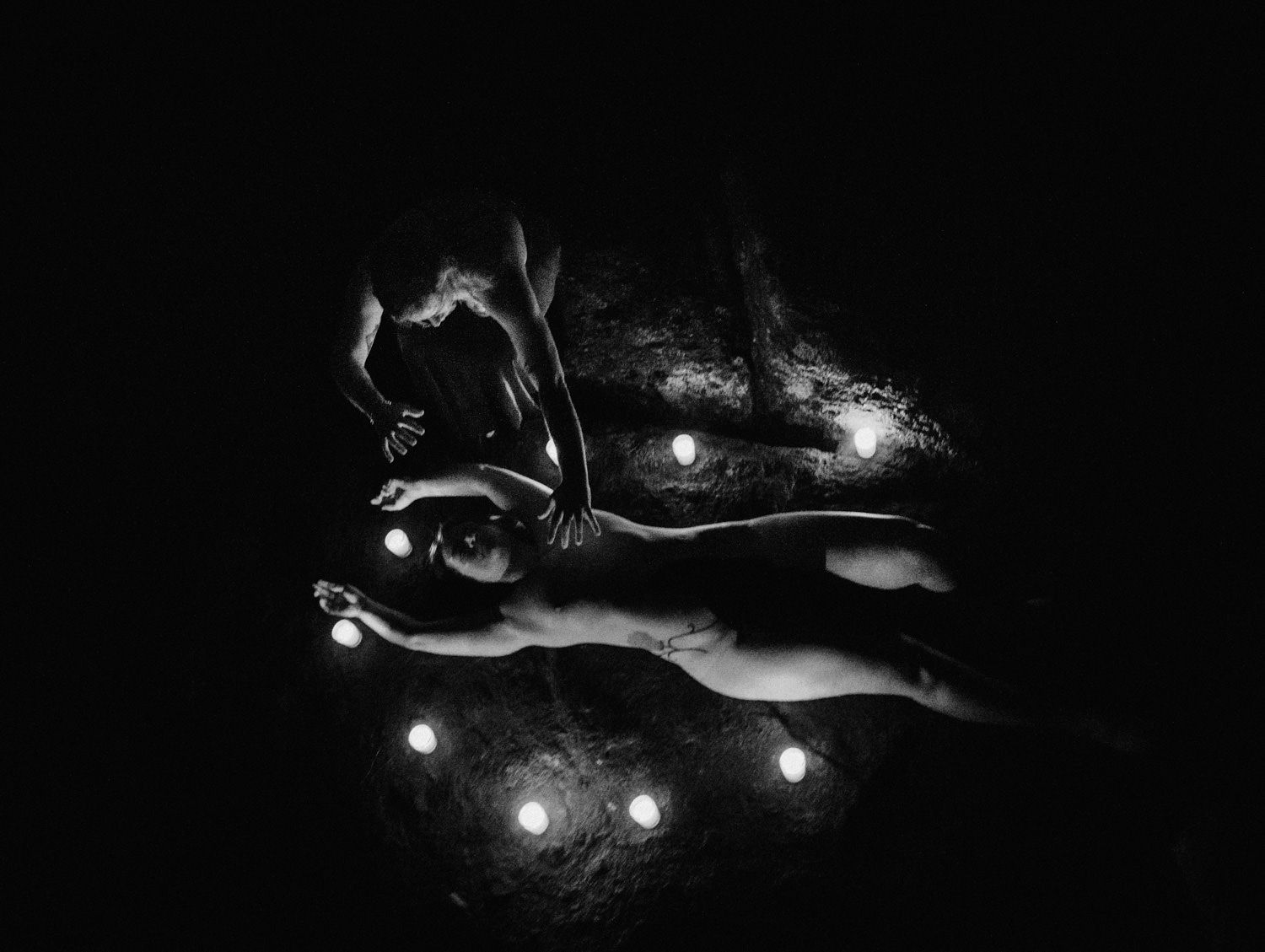 Black and white fine art photo of a figure lying on dark ground surrounded by glowing orbs of light.