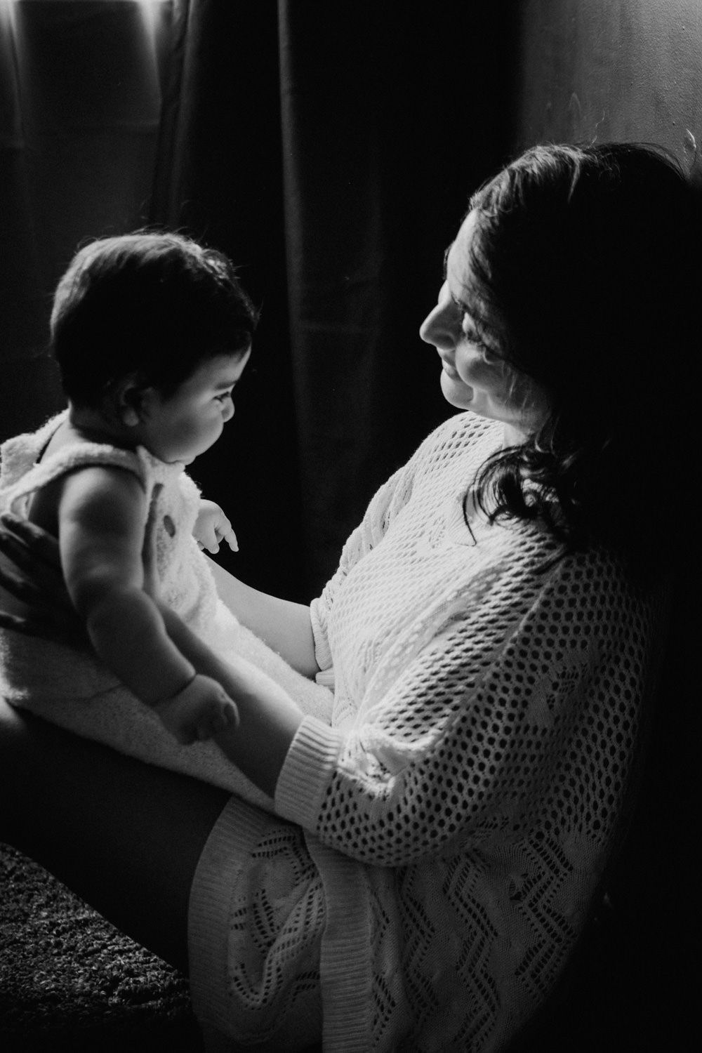 Black and white photo of a woman tenderly holding a baby, sharing a gentle moment in soft natural light.