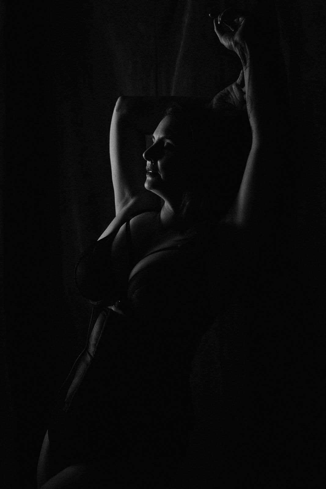 Black and white silhouette of a woman posing gracefully with arms raised against a dark background.