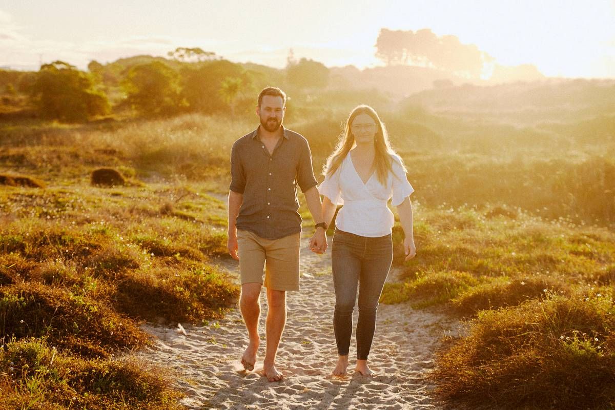 Couple holding hands walking on a scenic golden sunset path through lush green meadows.