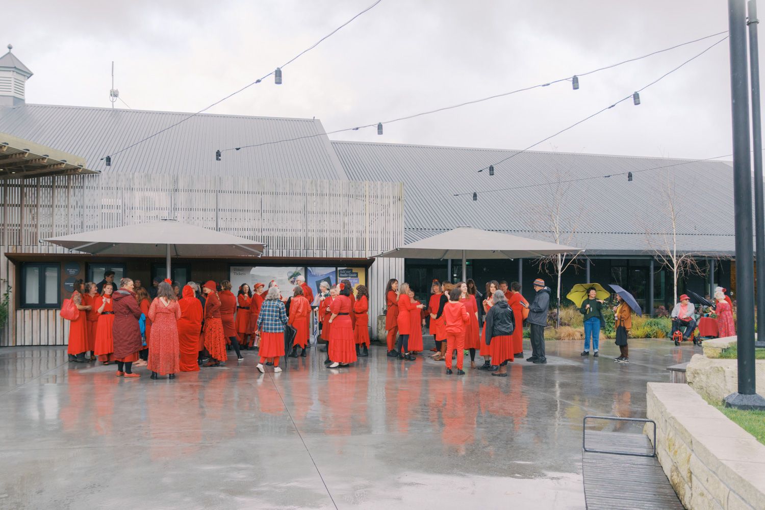 Group of people in red robes gathered outside a modern building on a rainy day.
