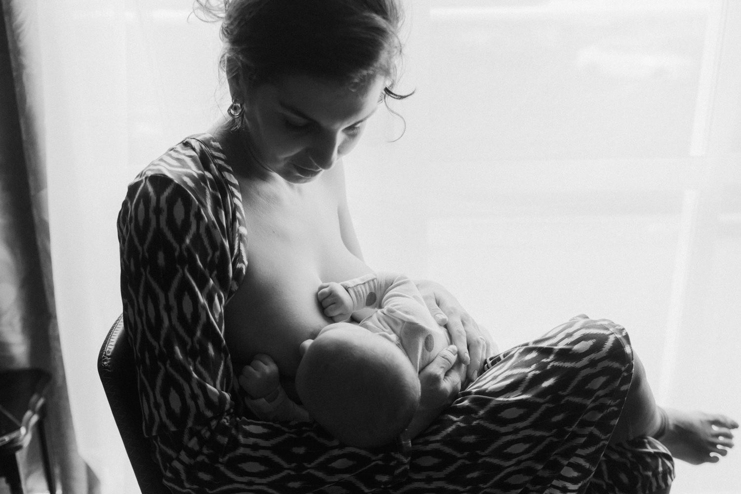 Black and white photo of a mother breastfeeding her newborn baby by a window.